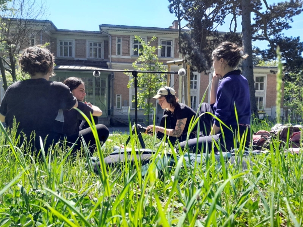 Studierende sitzen
                                          im Gras vor einem Gebäude