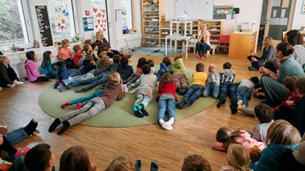 Kinder
                                          sitzen in einem Klassenzimmer am Boden vor einer Lehrerin