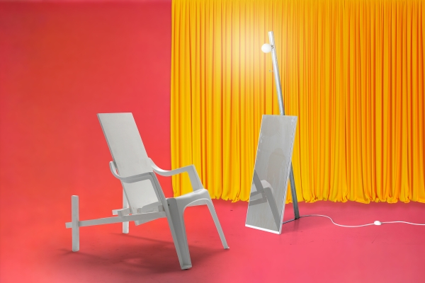 Ein weißer Designsessel
                                          steht vor einem beleuchteten Spiegel - im Hintergrund sieht man einen gelben Vorhang vor rosafarbener Wand.