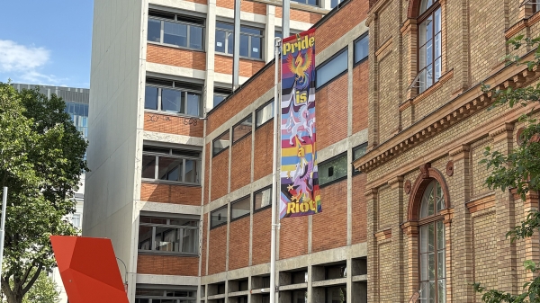 Eine Prideflagge
                                          vor der Universität für angewandte Kunst Wien. Darauf zu sehen ist ein Einhorn, ein Hippogreif und ein Phönix. Im Hintergrund
                                          gehen regenbogen-farbene Streifen ineinander über.