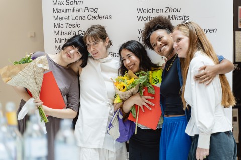 Ein Gruppenfoto von vier Abolsvent*innen vor dem Banner der Angewandte Abschlussarbeiten des Sommersemesters 2026