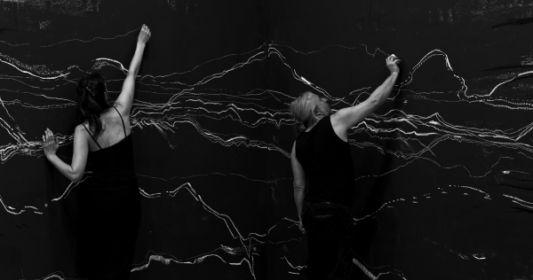 Ein Mann und eine Frau in
                                          schwarz gekleidet zeichnen helle Linien auf einer dunklen Wand