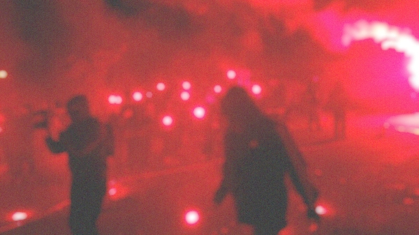 A blurry photograph showing
                                          people, red fireworks and smoke.